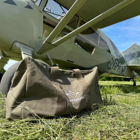 Brown duffel bag with a logo on the grass in front of a small airplane