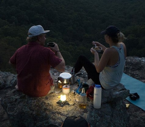 Two people sitting on a rocky outcrop at night, enjoying drinks and snacks.