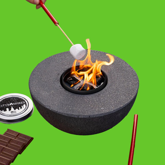 Person roasting marshmallows over a portable fire pit on a wooden surface.