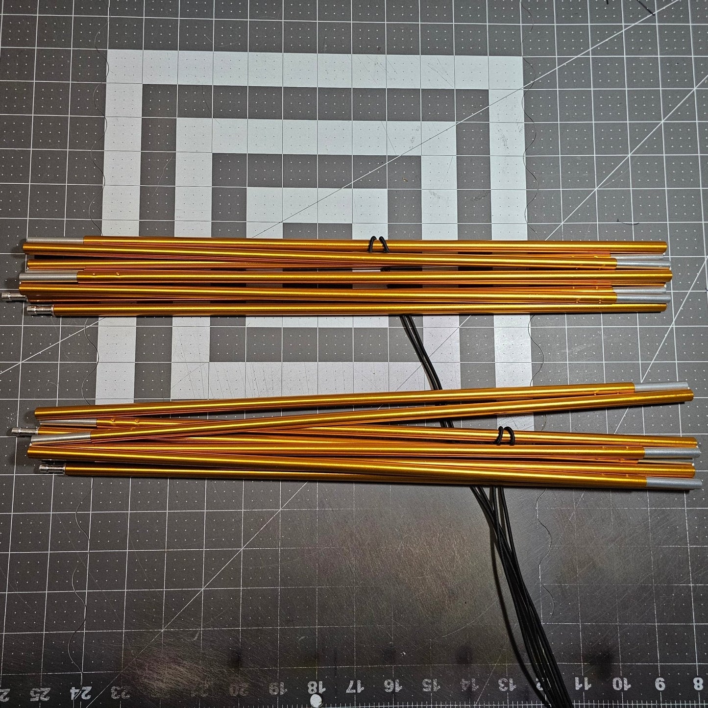 Gold metal rods on a gray cutting mat with grid lines