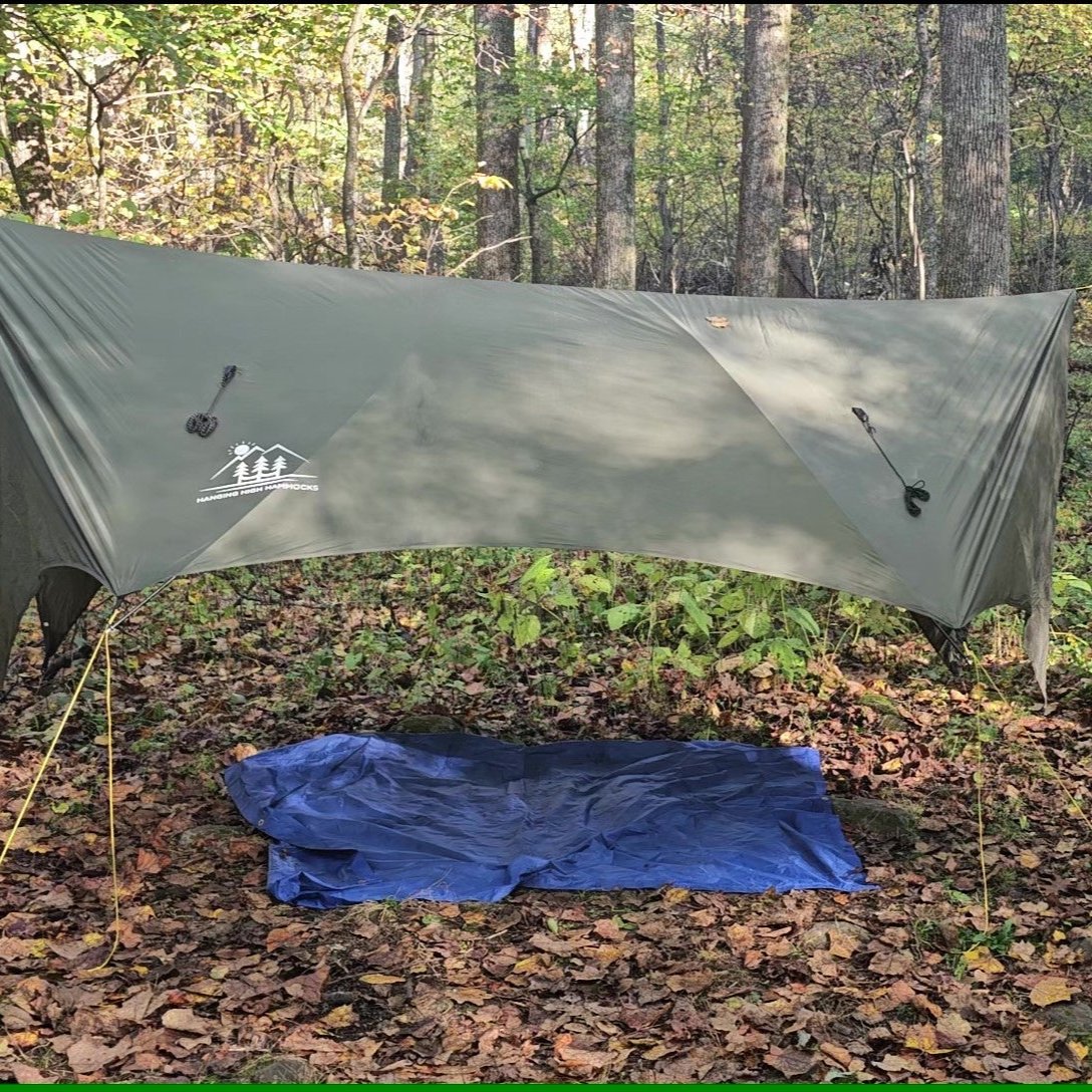 Green tarp set up in a forest with a blue sleeping bag underneath