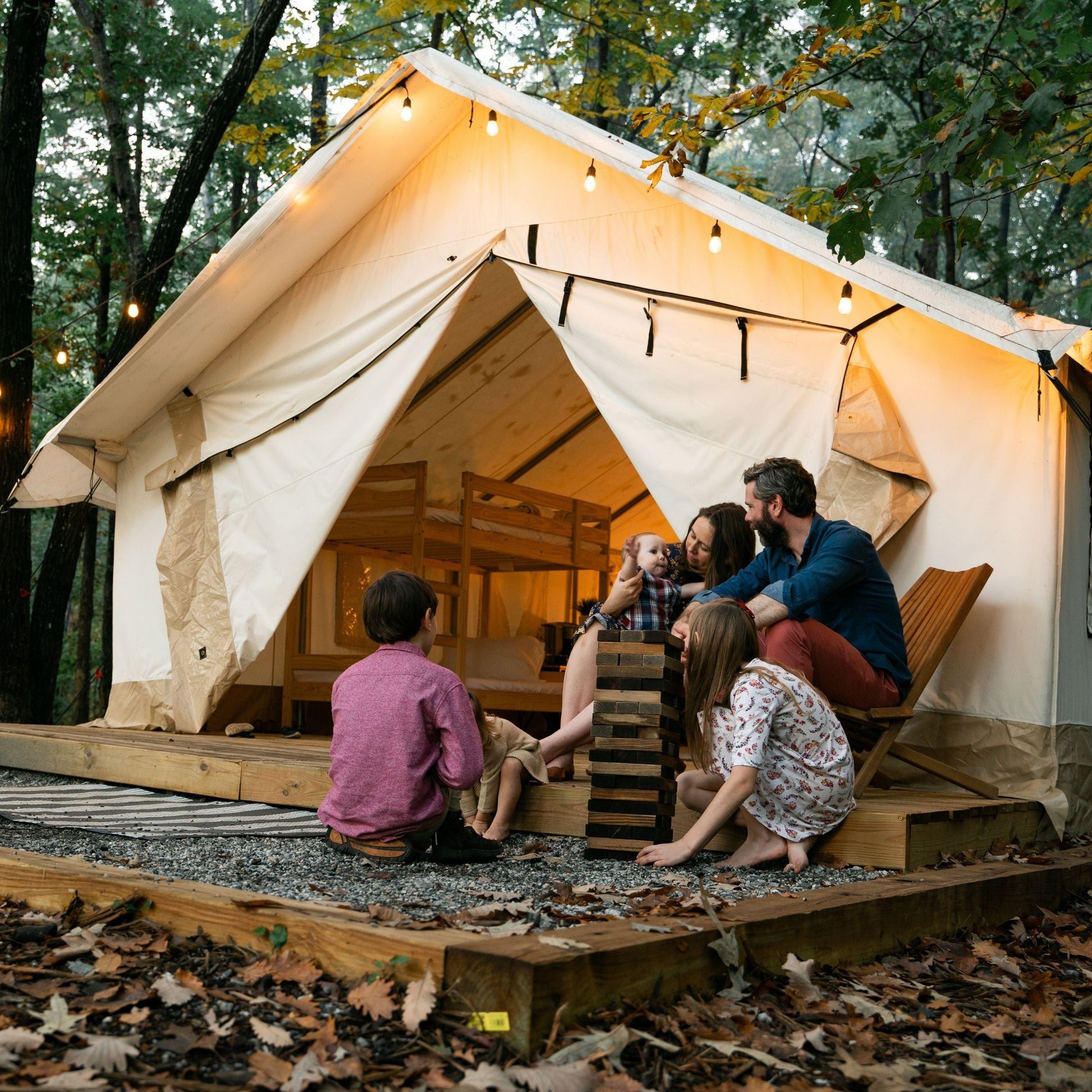 Family sitting outside a large illuminated tent in a forest setting