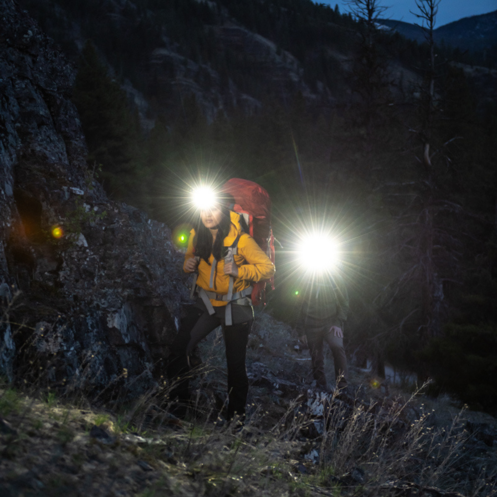Person with a backpack and headlamps in a dark forest
