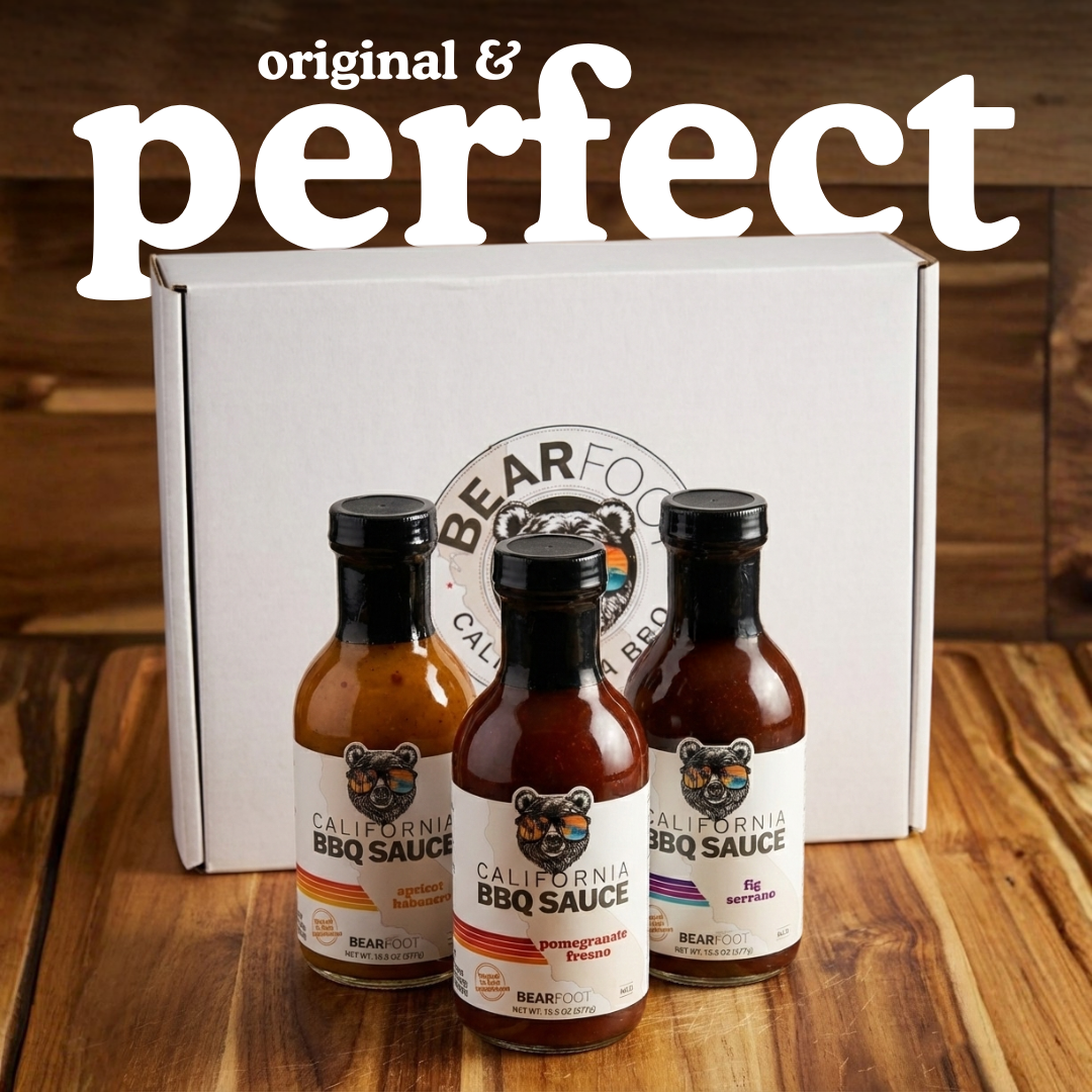 Three bottles of Bearfoot California BBQ Sauce in front of a branded box on a wooden surface.