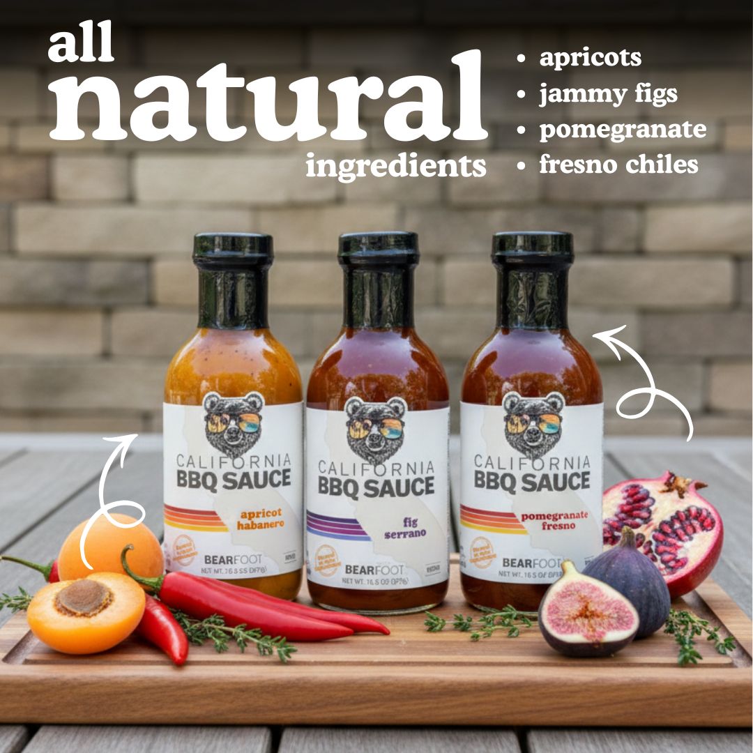 Three bottles of California BBQ Sauce on a wooden board with fruits and chilies, labeled 'all natural ingredients'.