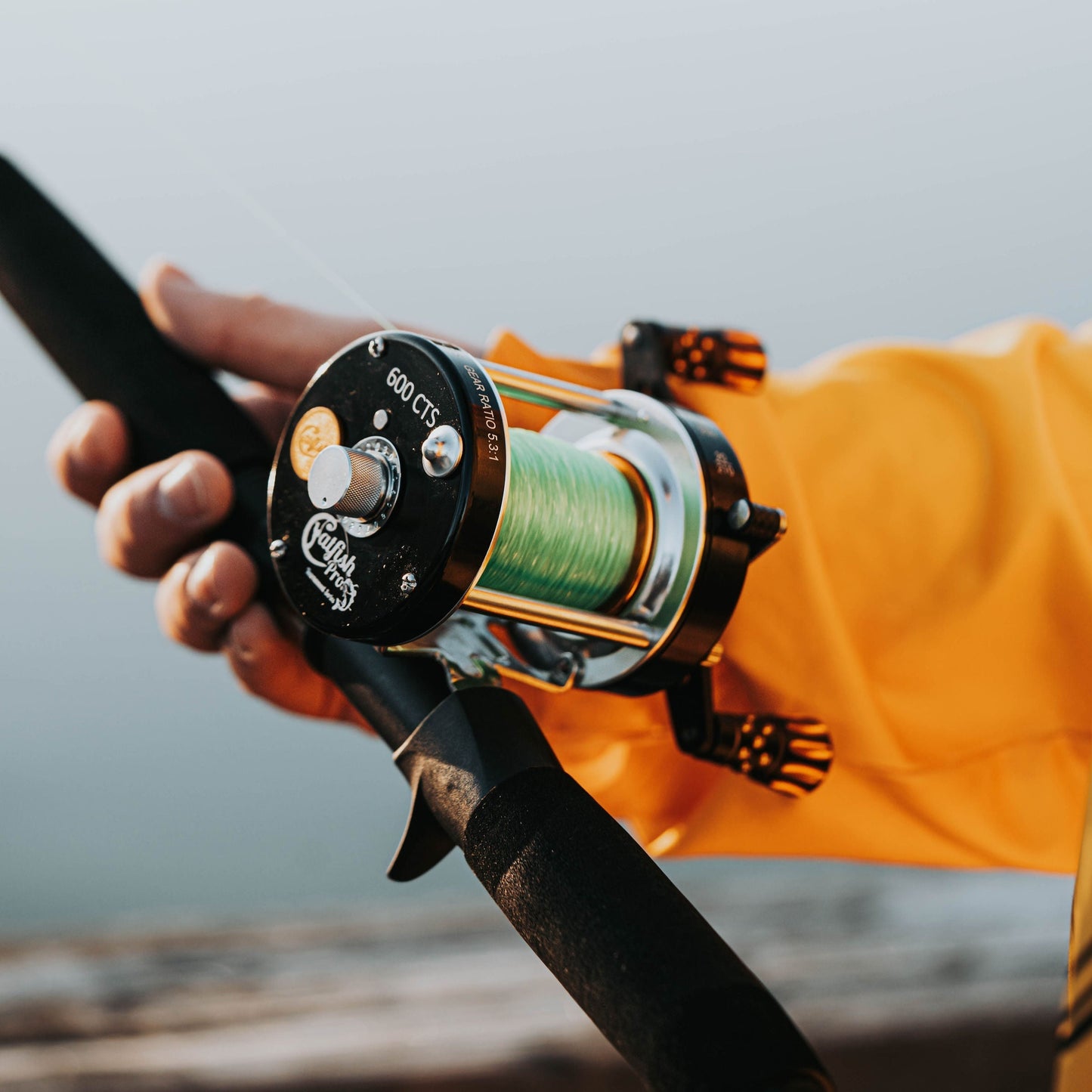 Fishing reel held by a person wearing an orange jacket with a blurred background