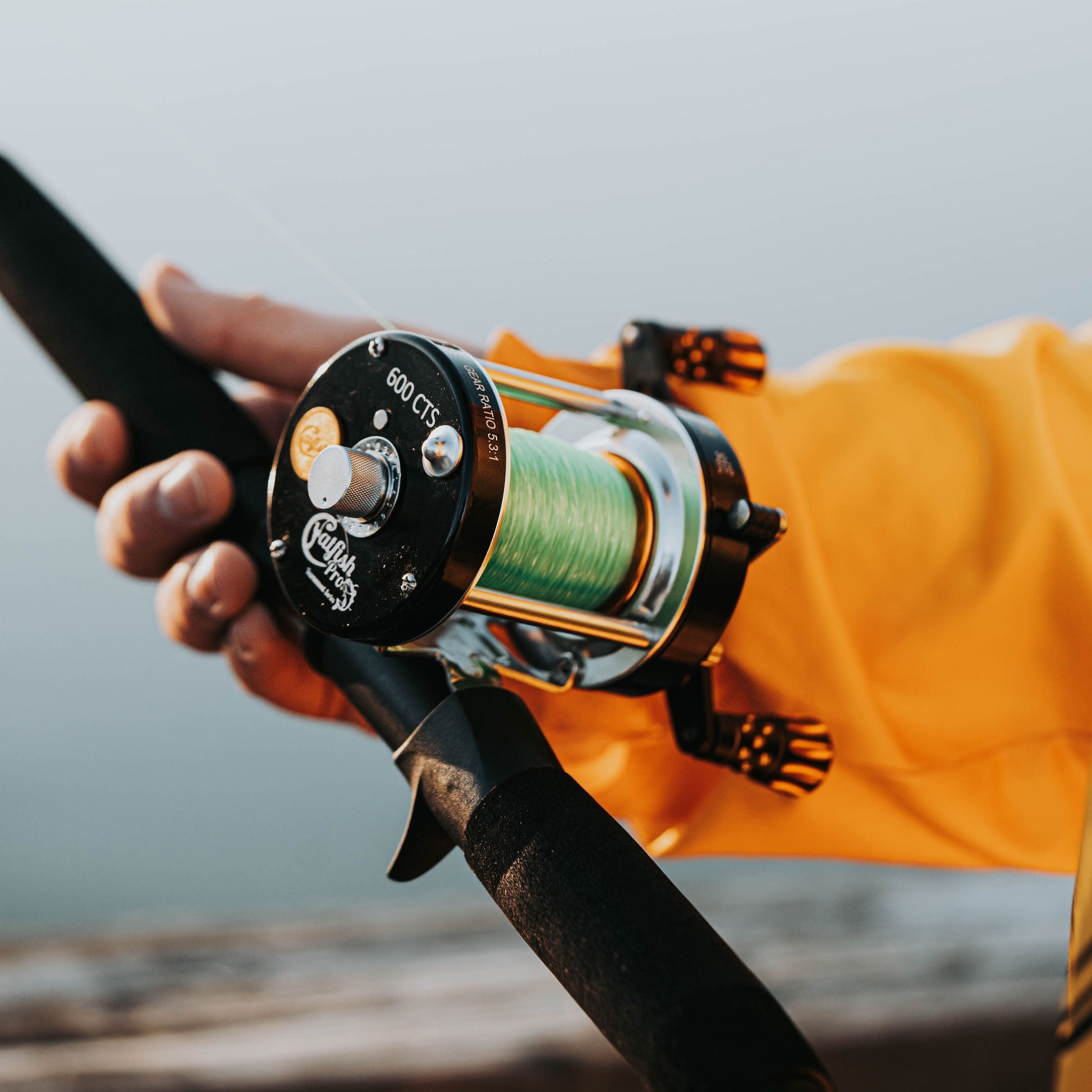 Fishing reel held by a person wearing an orange jacket with a blurred background