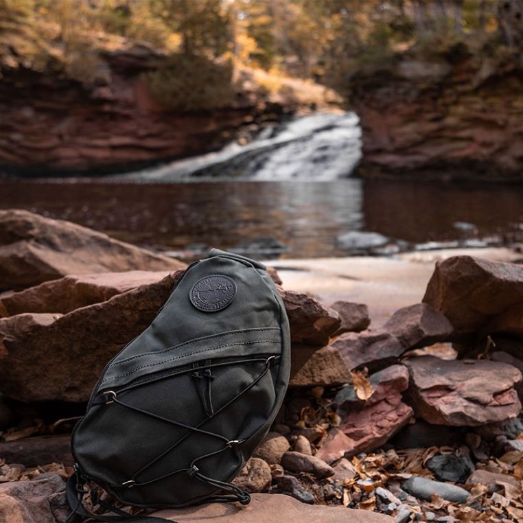 Black backpack on rocks with a waterfall in the background