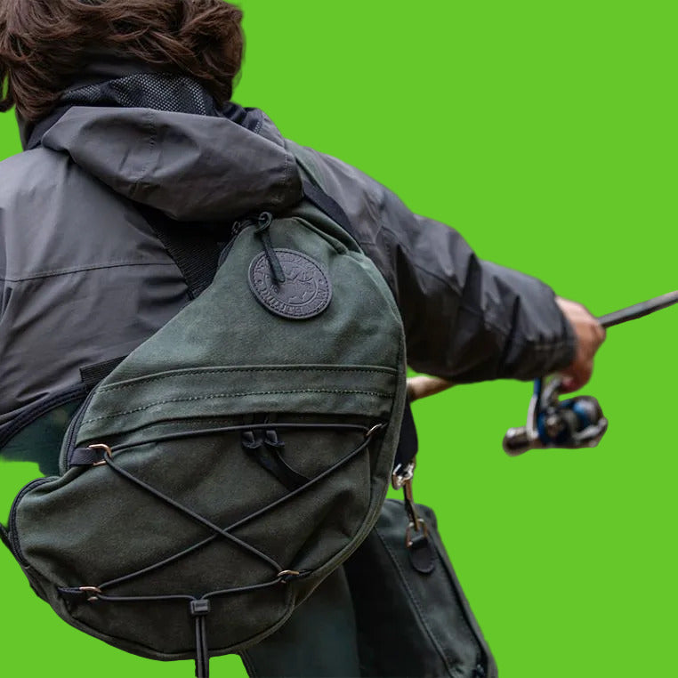 Person fishing with a green backpack by a body of water