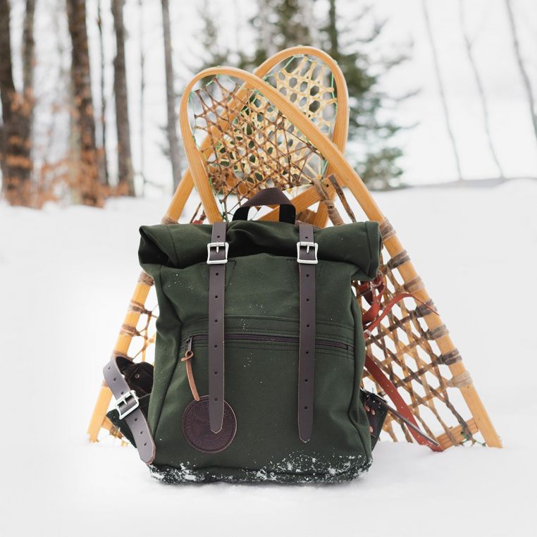 Green backpack with brown straps on snow, with snowshoes in the background