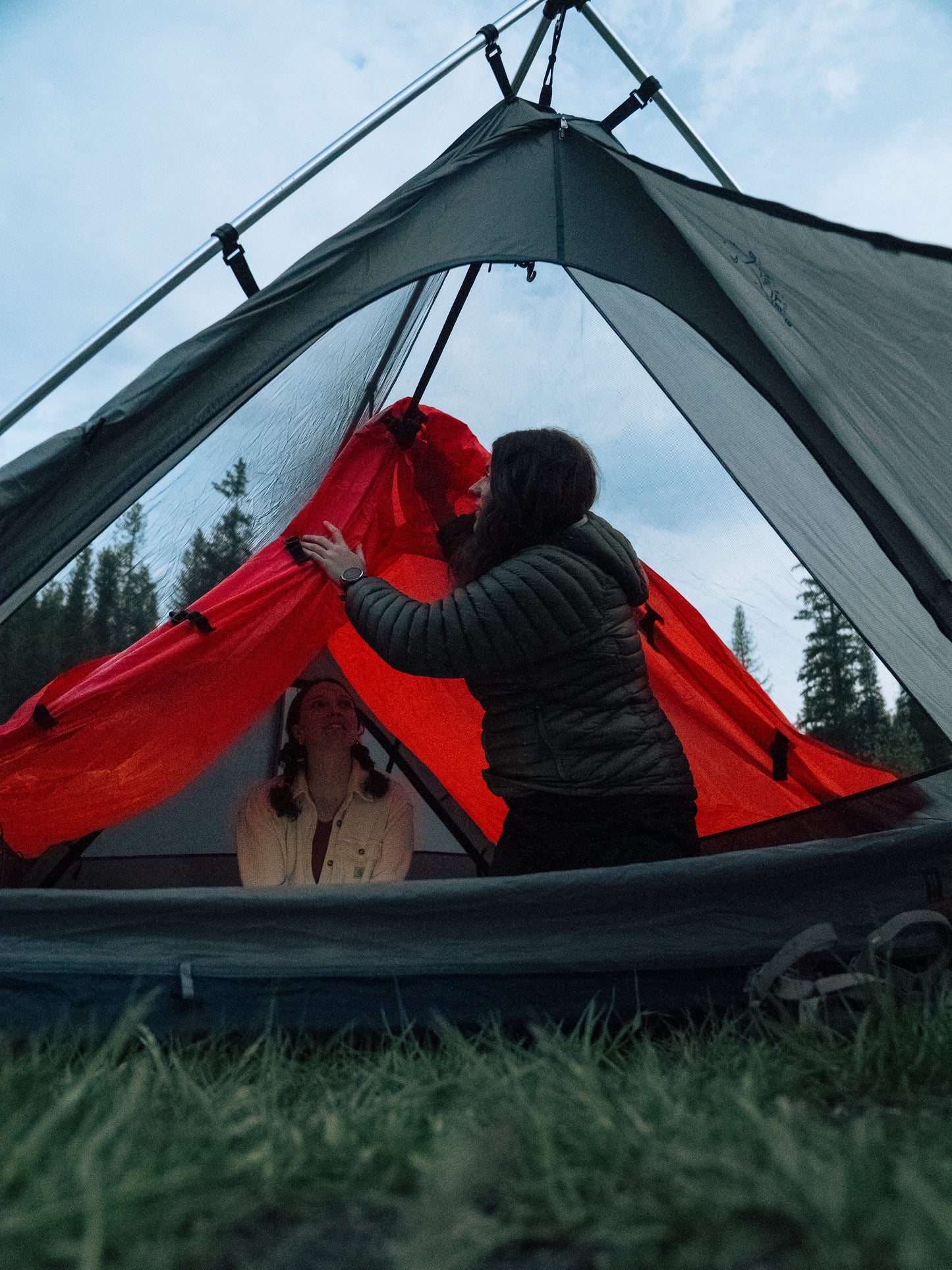 Two people setting up a tent with red interior in a forest setting