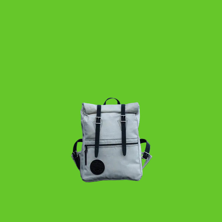 White backpack with black straps on a rocky beach near water and trees
