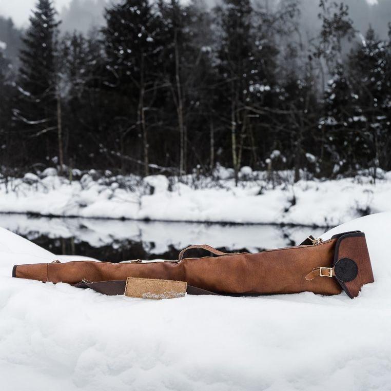 Brown leather bag on snow with a forest and lake in the background