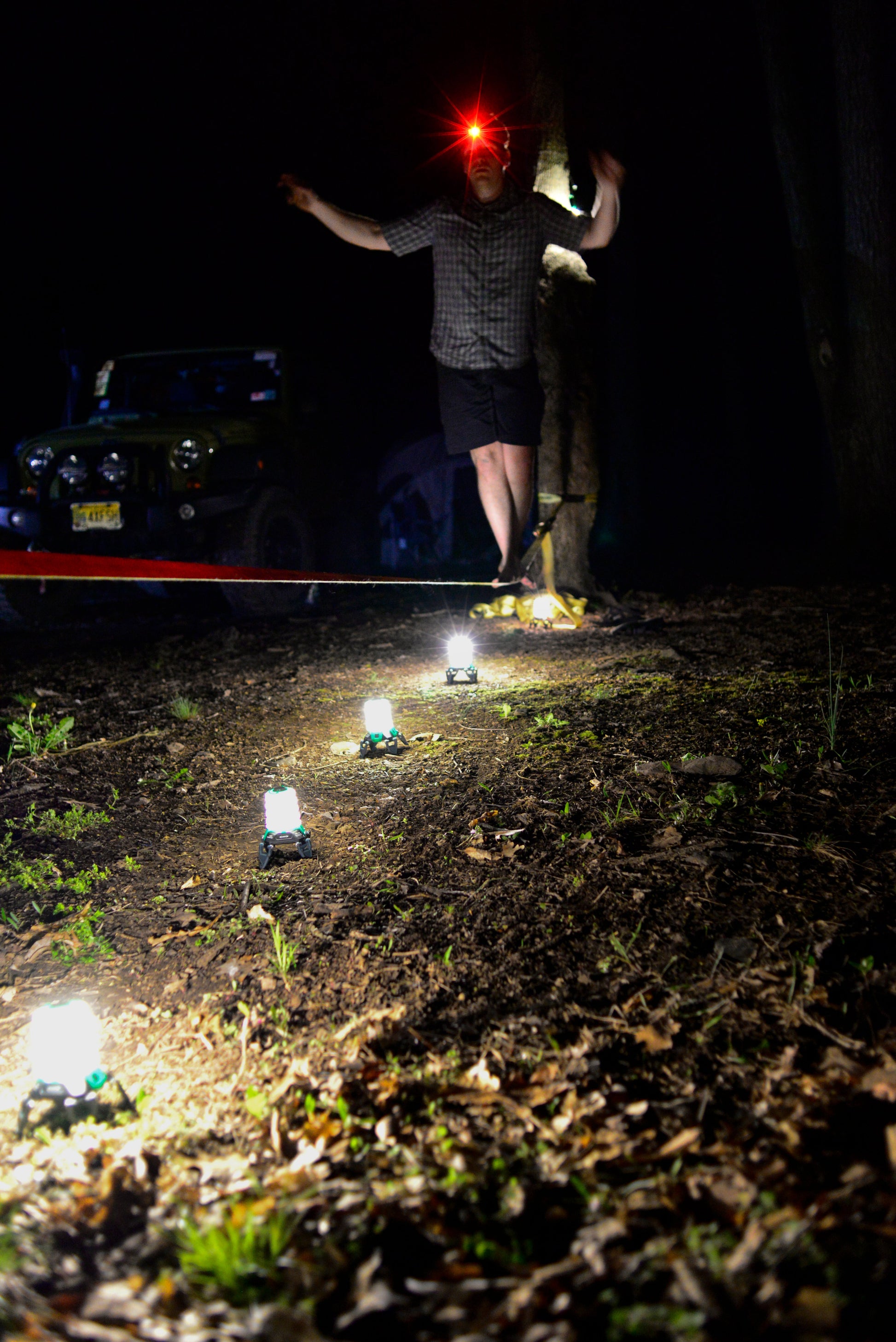 Person standing on a dirt road at night with vehicle lights illuminating the scene