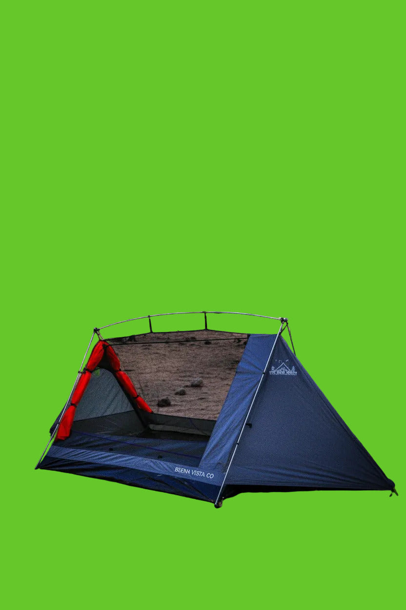 Camping tent set up in a forest with trees and blue sky in the background