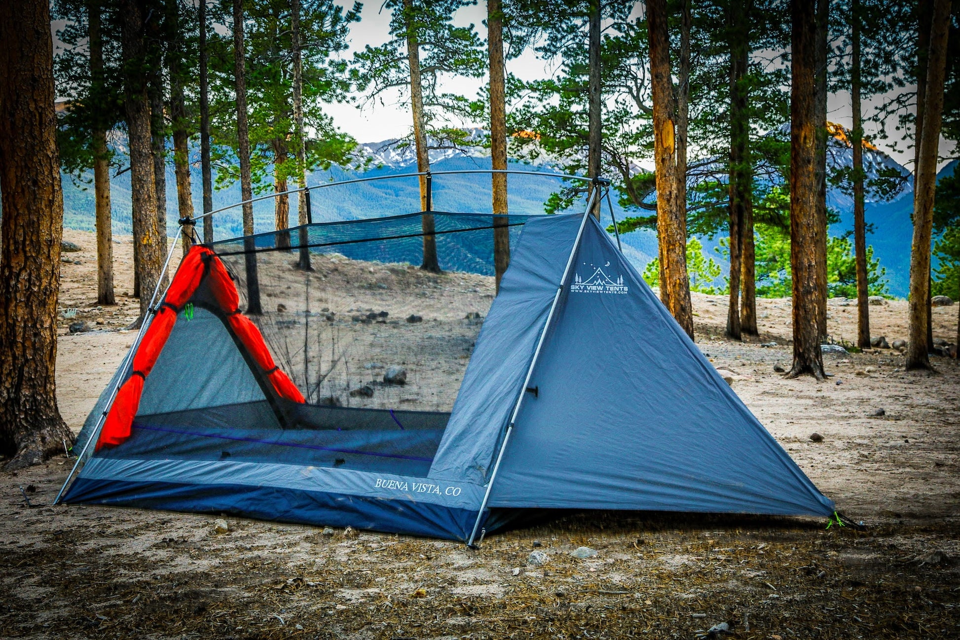 Blue camping tent with red accents set up in a forested area.
