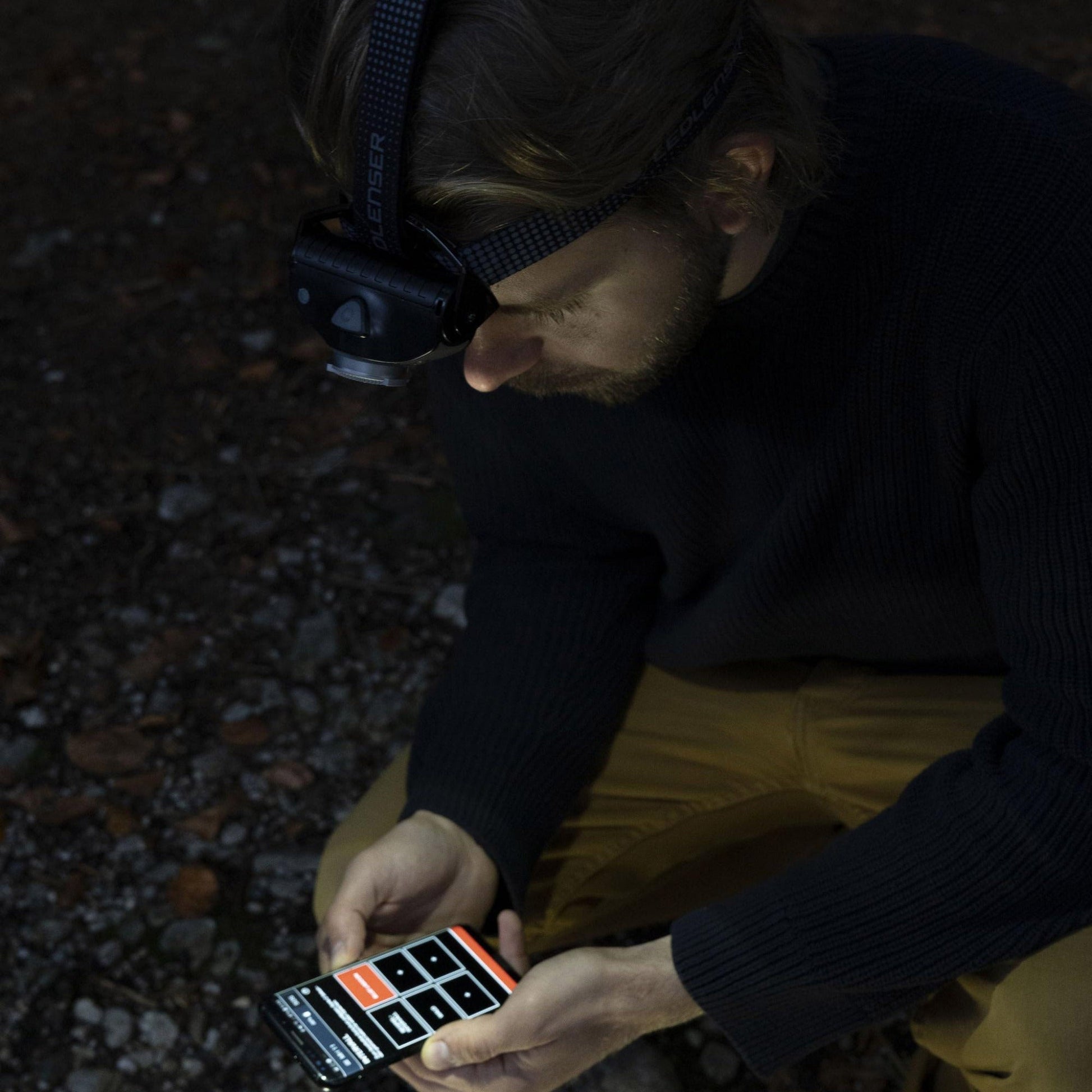 Person using a smartphone with a headlamp in a dark setting