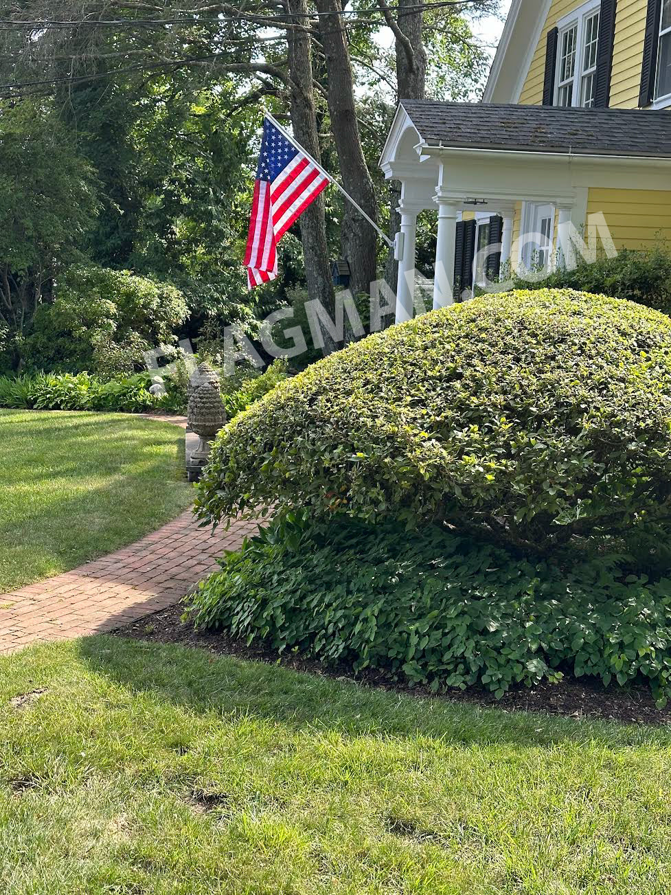 American flag waving in front of a house with a well-maintained garden.