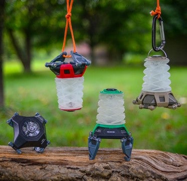 Three hanging camping lanterns with carabiners on a wooden log outdoors.
