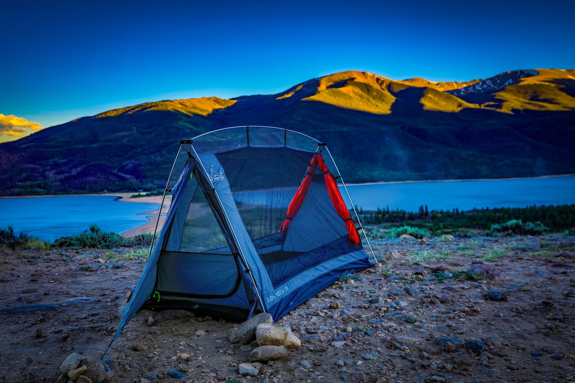 Camping tent set up near a lake with mountains in the background