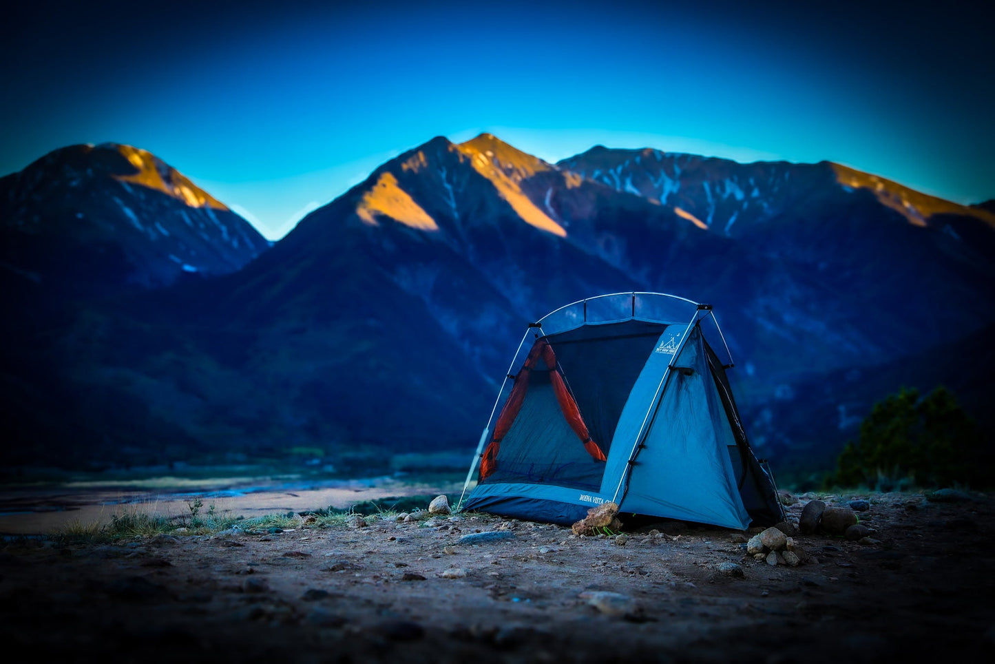 Blue camping tent in front of a mountain range at dusk