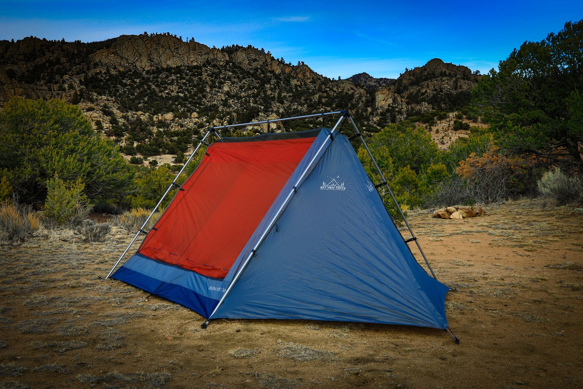 Red and blue tent set up in a desert landscape with mountains in the background