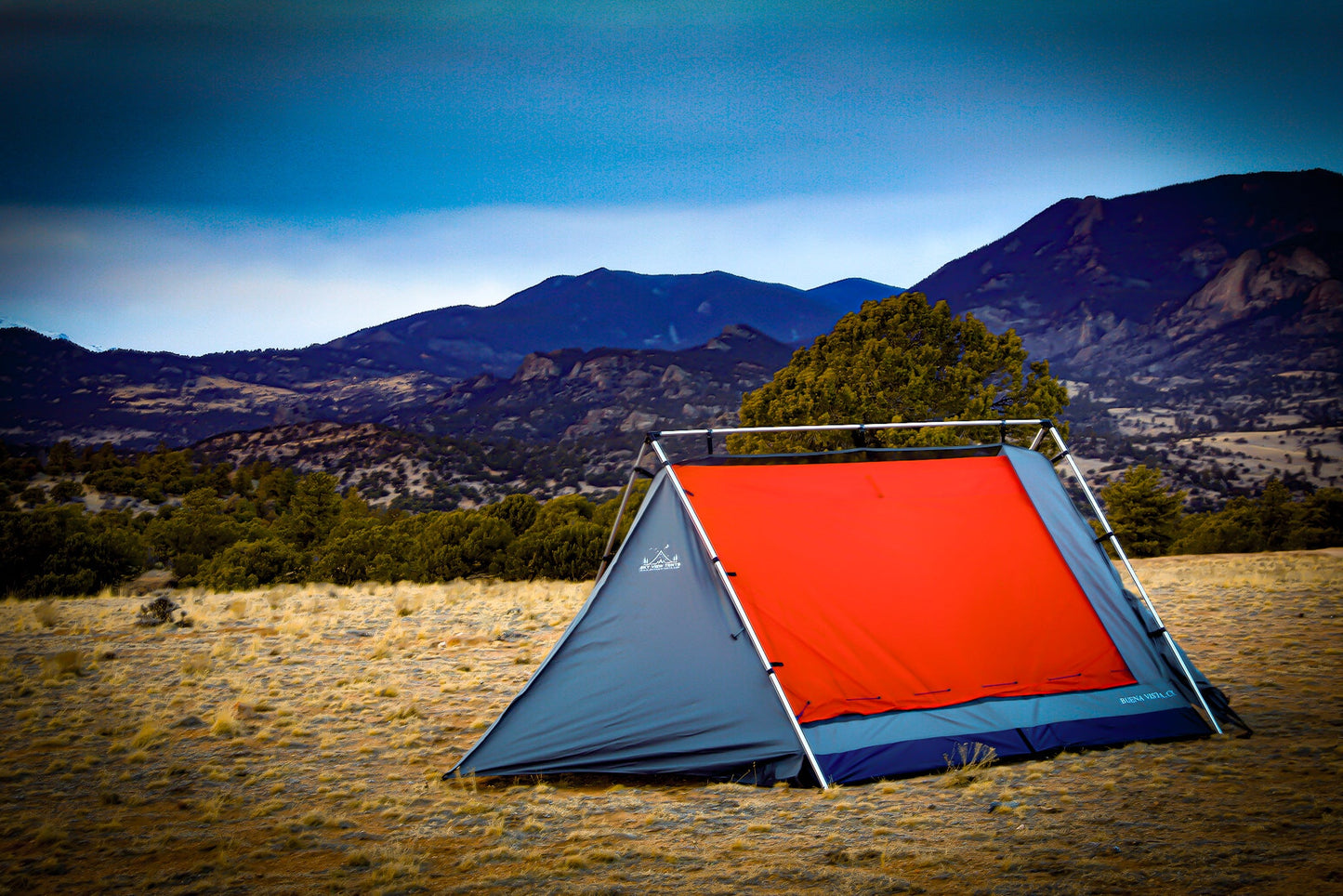 Camping tent with red flap in a field with mountains in the background