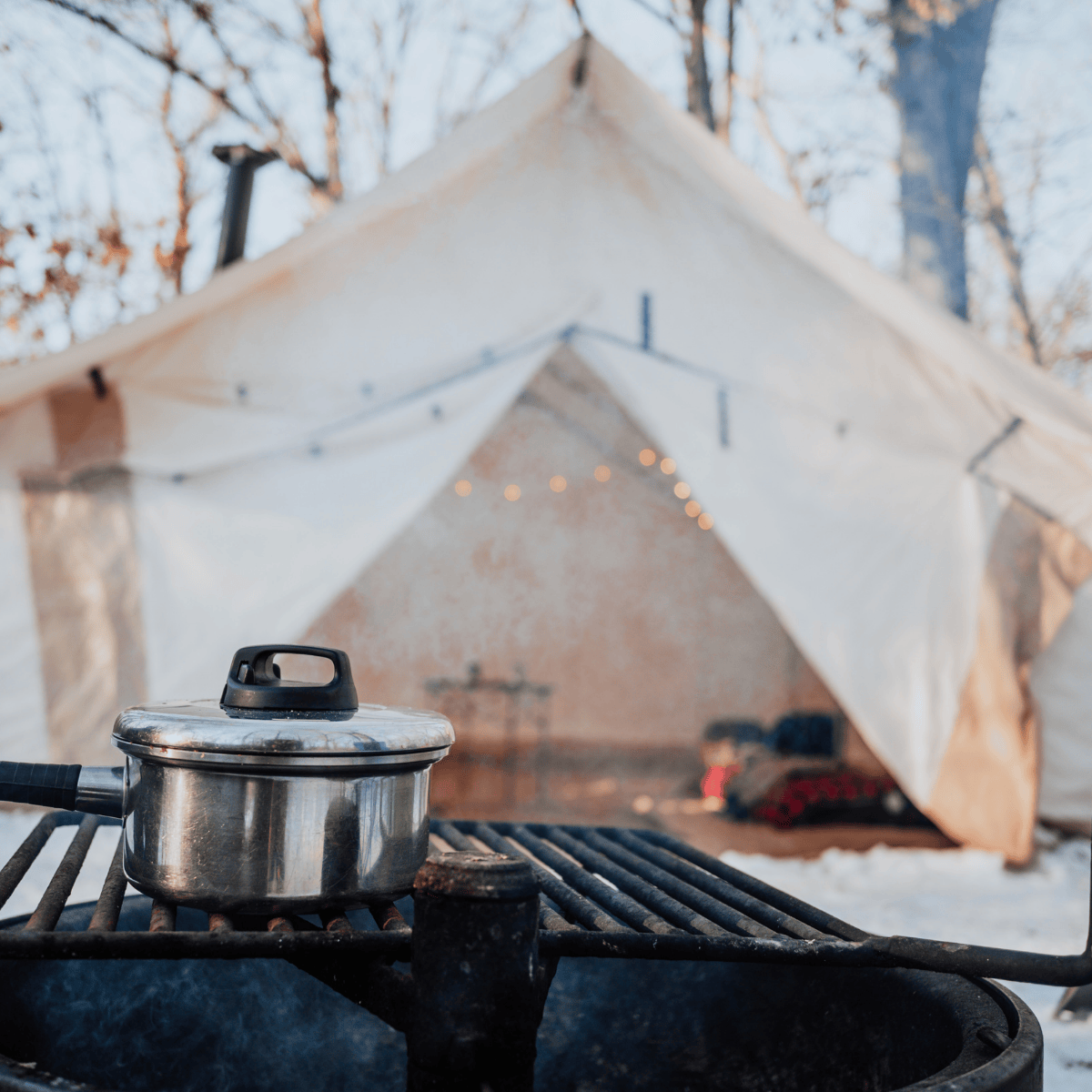Camping scene with a pot on a stove in front of a tent in a snowy landscape.