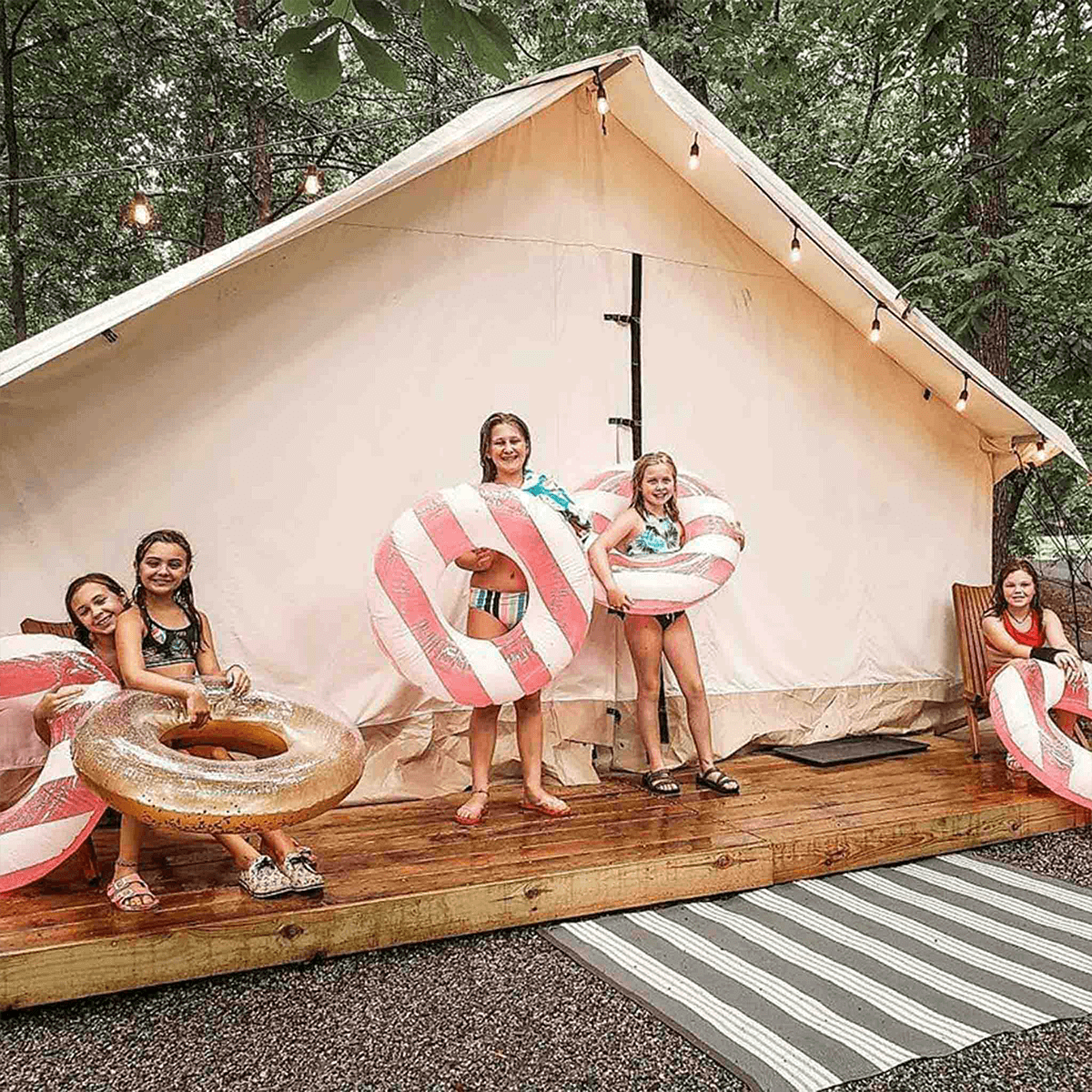 Children with inflatable rings on a wooden deck in front of a large tent.