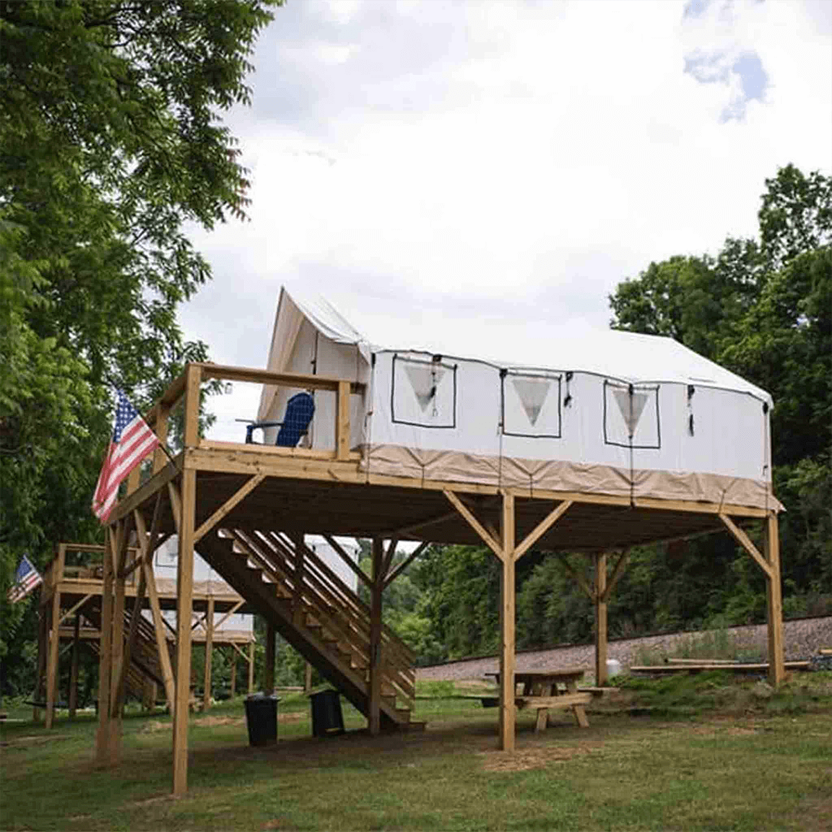 Yurt with a wooden platform and stairs, surrounded by trees and American flags.
