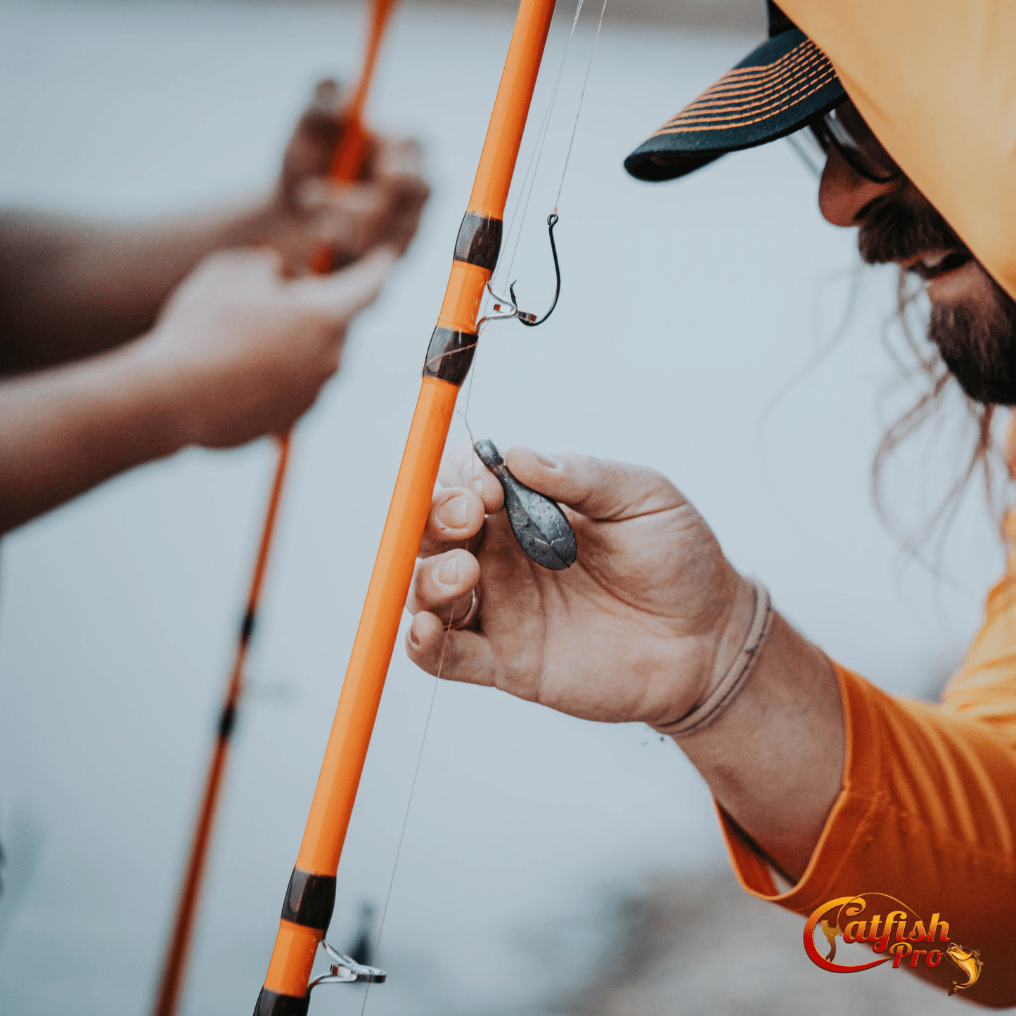 Person adjusting a fishing rod with another person in the background, both outdoors.