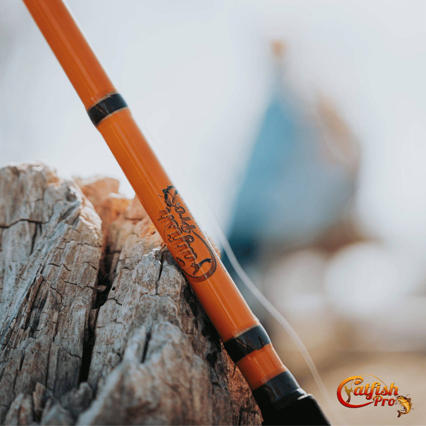 Orange fishing rod with black accents leaning against a wooden log, blurred background
