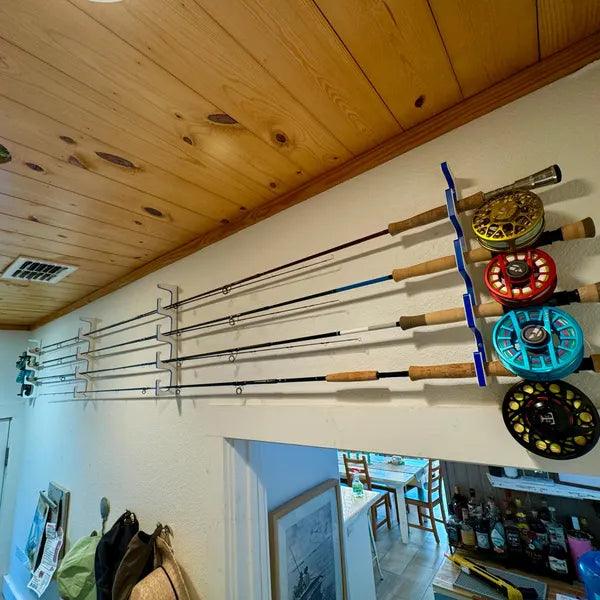 Fishing rods and reels on a wall-mounted holder in a room with wooden ceiling and white walls.