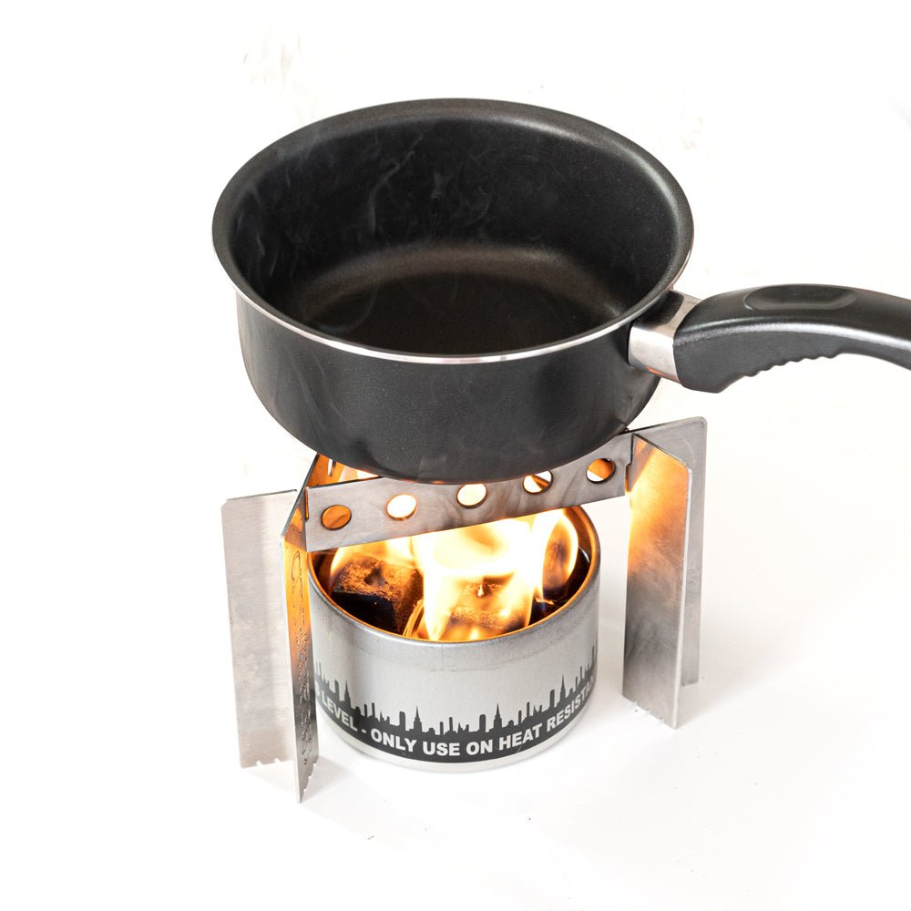 Black frying pan on a small stove with flames underneath, on a white background