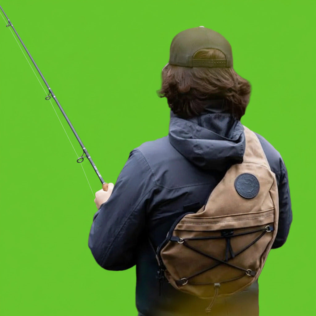 Person fishing with a brown bag over their shoulder by a body of water.