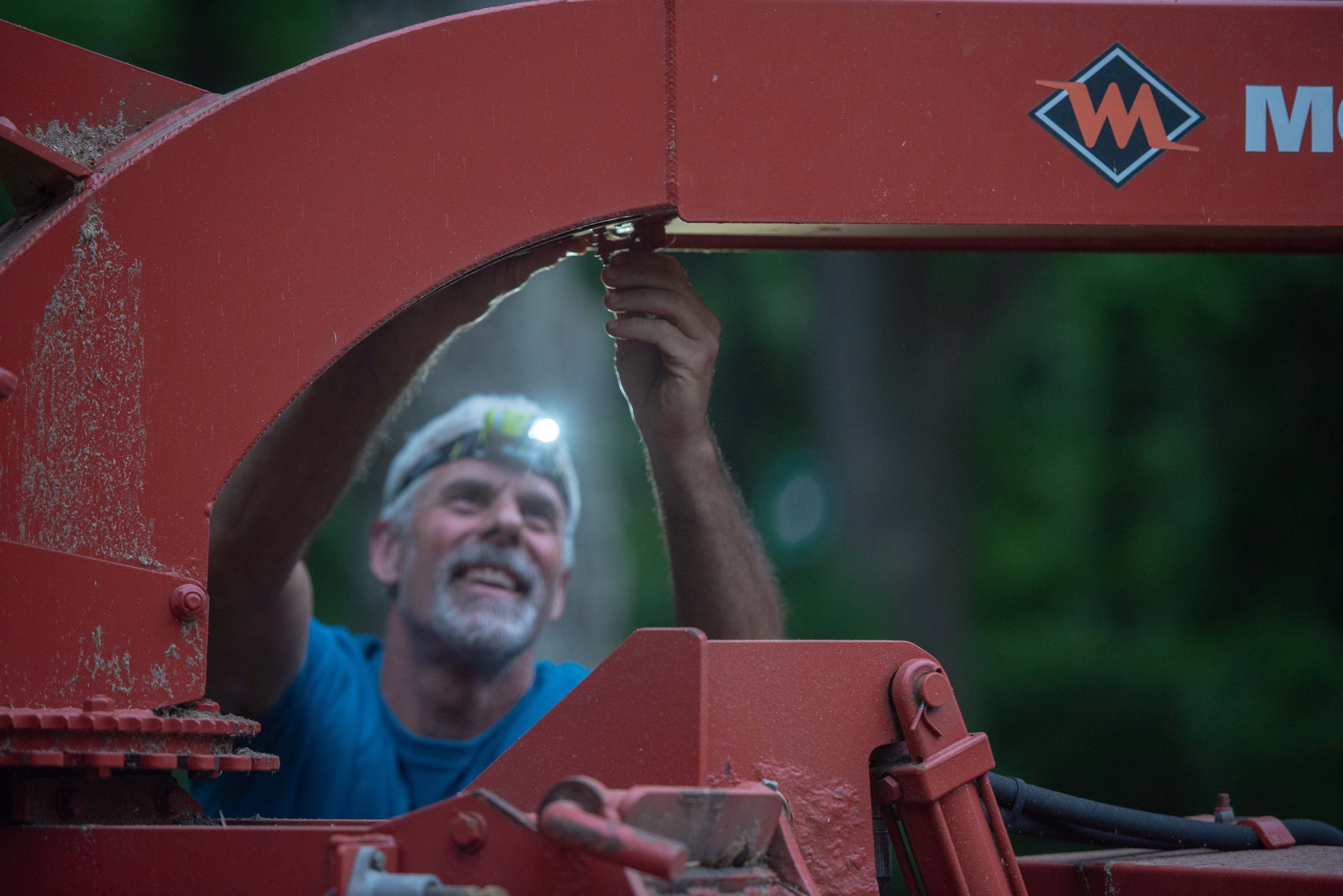 Man working on a large red piece of machinery with a visible brand logo.