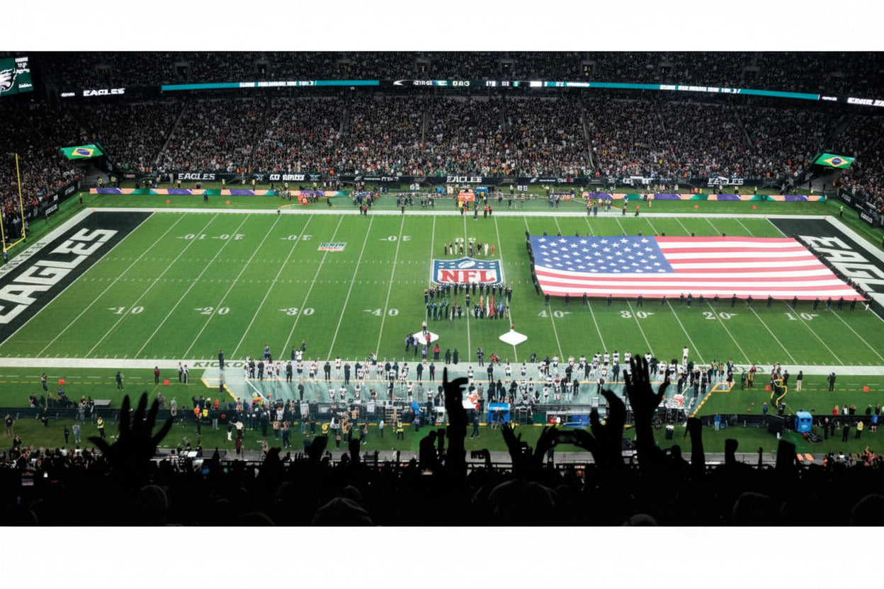 Large American  flag on a football field with spectators in the stands.