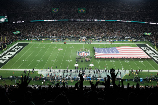 Large American  flag on a football field with spectators in the stands.