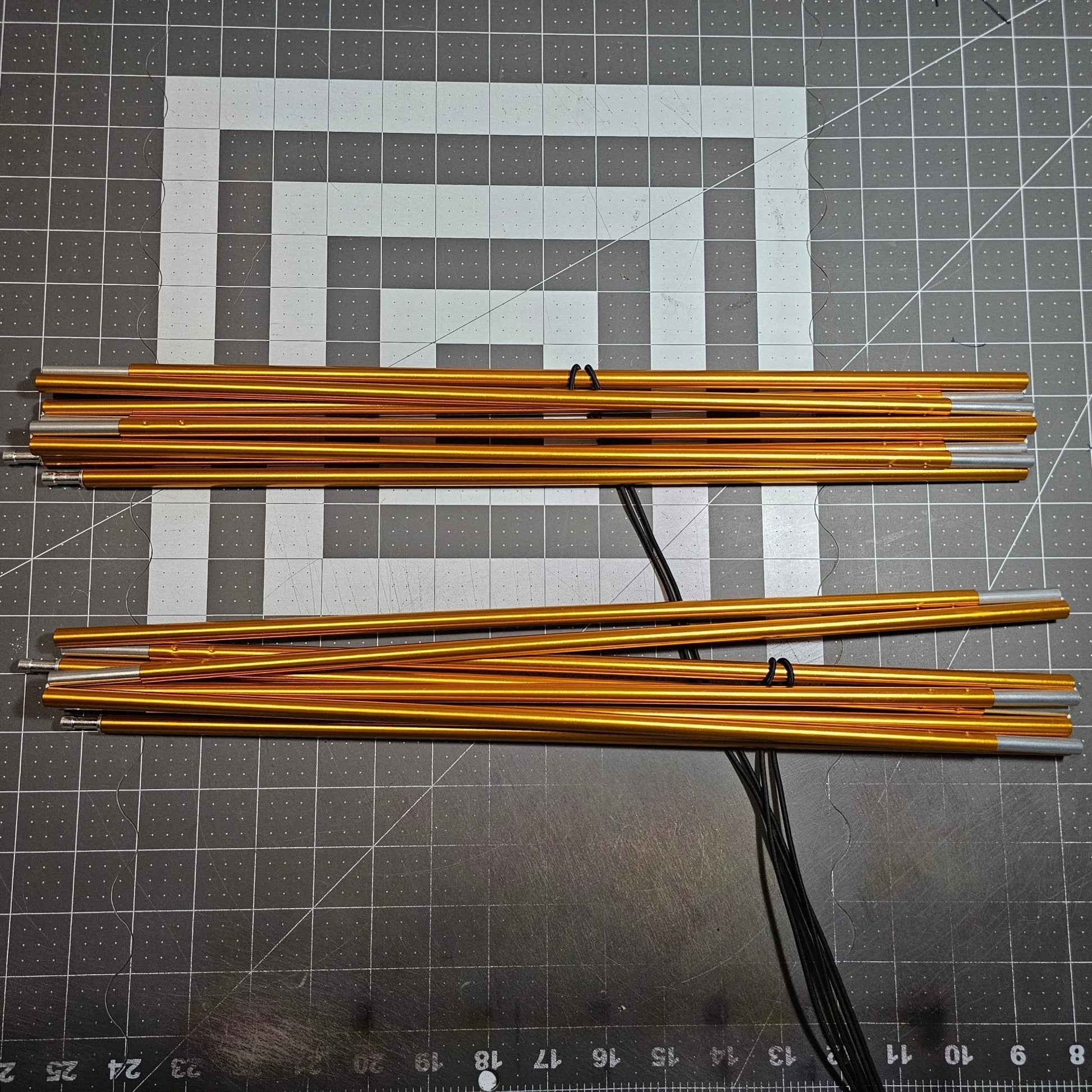 Gold metal rods on a gray cutting mat with grid lines